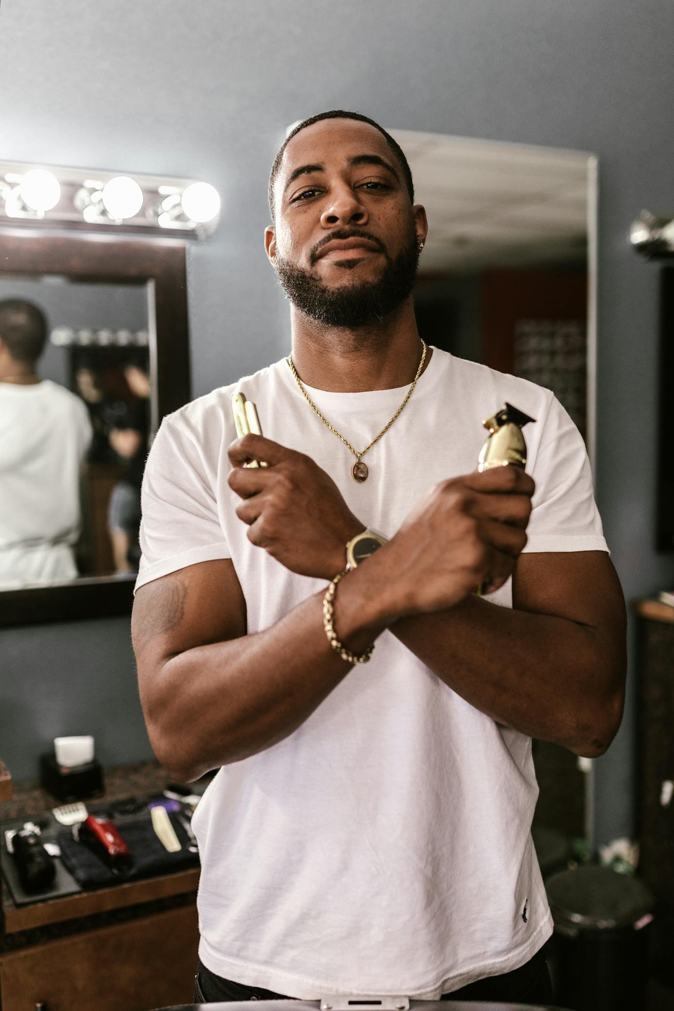 A stylish barber confidently holds hair clippers in a modern barbershop setting.