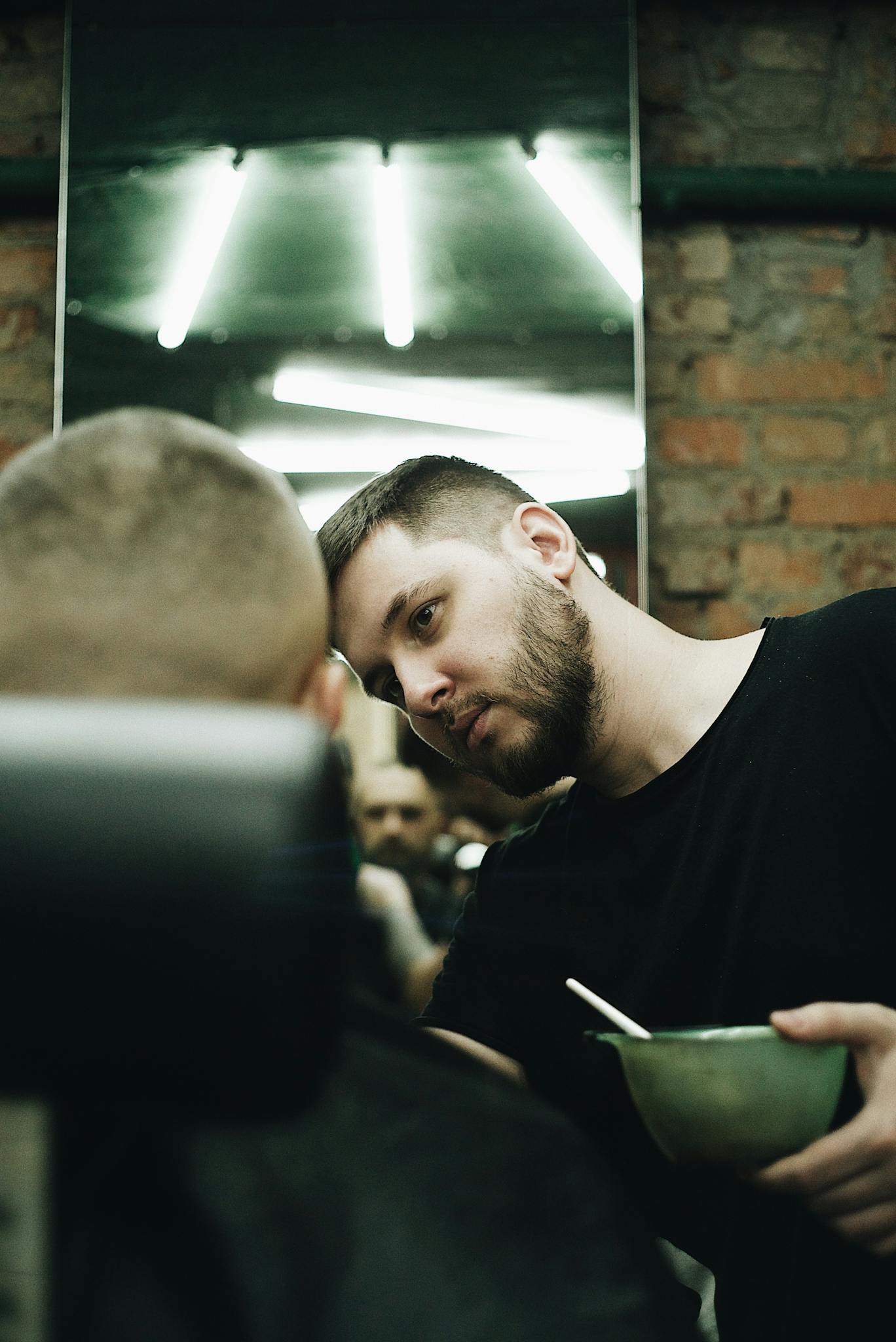 Barber focuses on grooming a client's hair in a stylish urban salon with exposed brick and neon lighting.