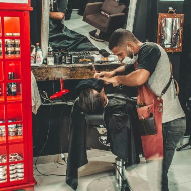 Barber performing a haircut in a stylish barbershop with a mirror reflection.
