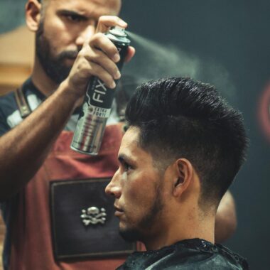 Experienced stylist applies finishing spray to client's hair during grooming session at modern barbershop.