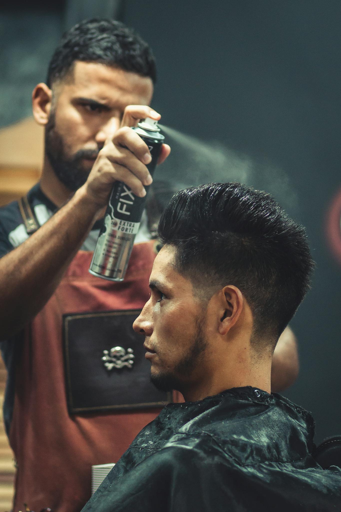 Experienced stylist applies finishing spray to client's hair during grooming session at modern barbershop.